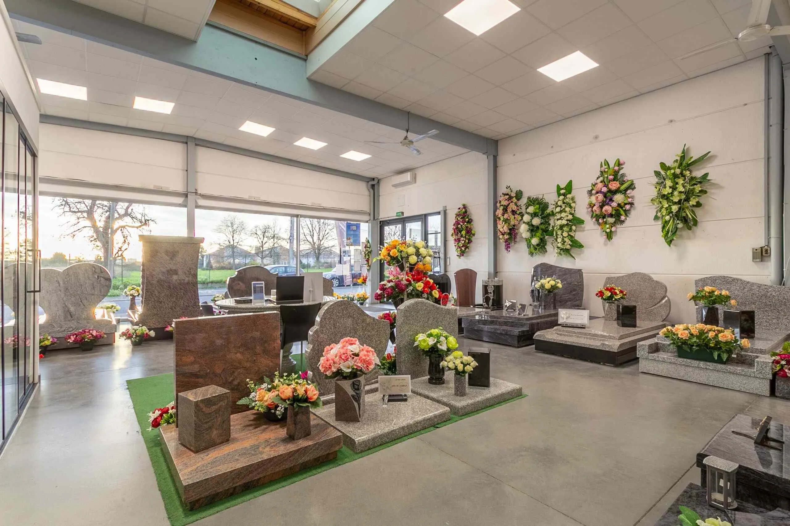 Intérieur du magasin de marbrerie funéraire présentant des monuments, plaques et compositions florales